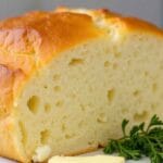 Freshly baked cottage cheese loaf sliced on a wooden board with butter and herbs