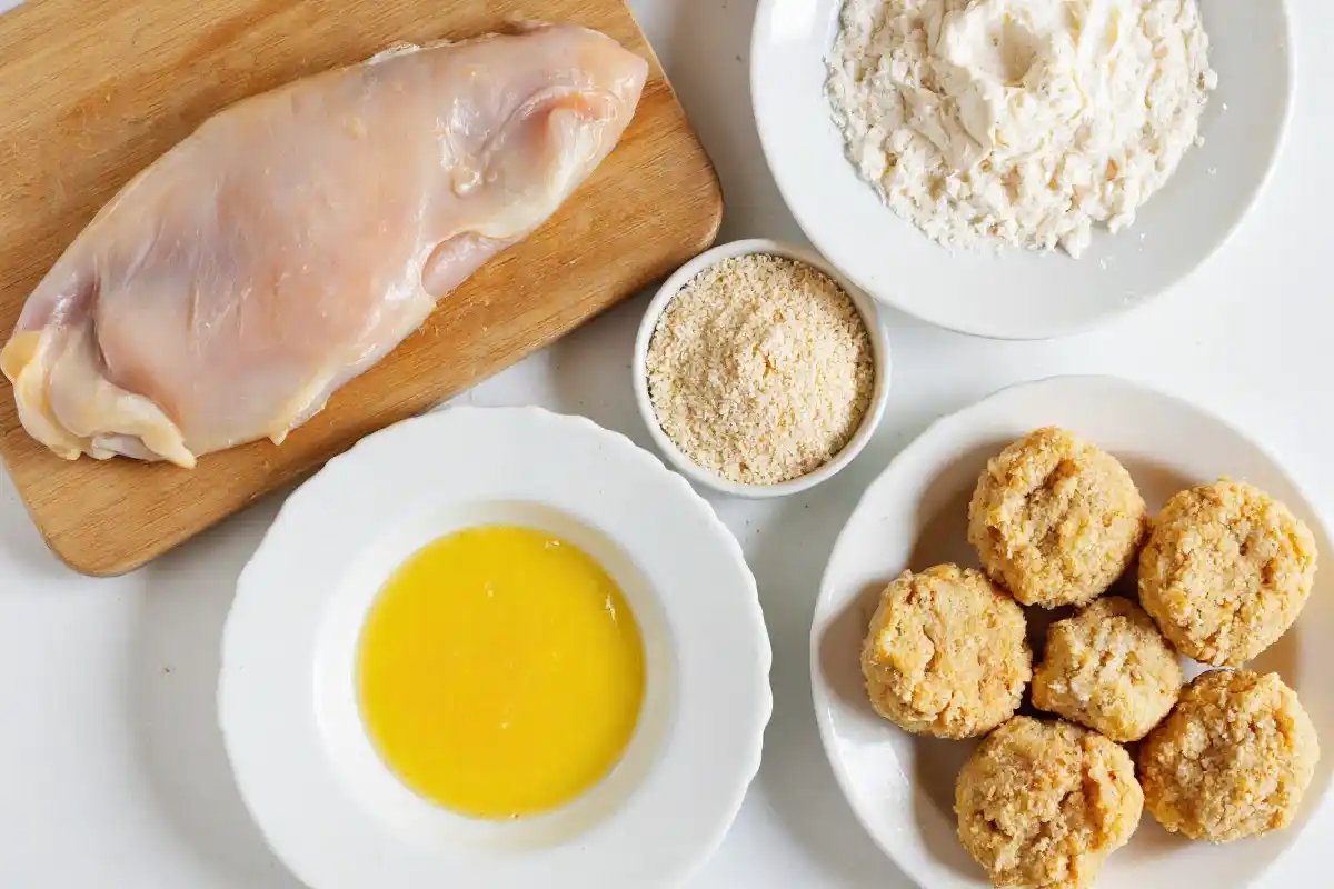 Ingredients For The Best Homemade Chicken Nuggets Recipe Raw chicken breast, eggs, flour, and breadcrumbs arranged on a kitchen counter.