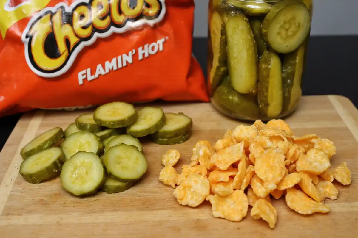 Fresh dill pickles and a bag of Flamin’ Hot Cheetos arranged on a wooden table.
