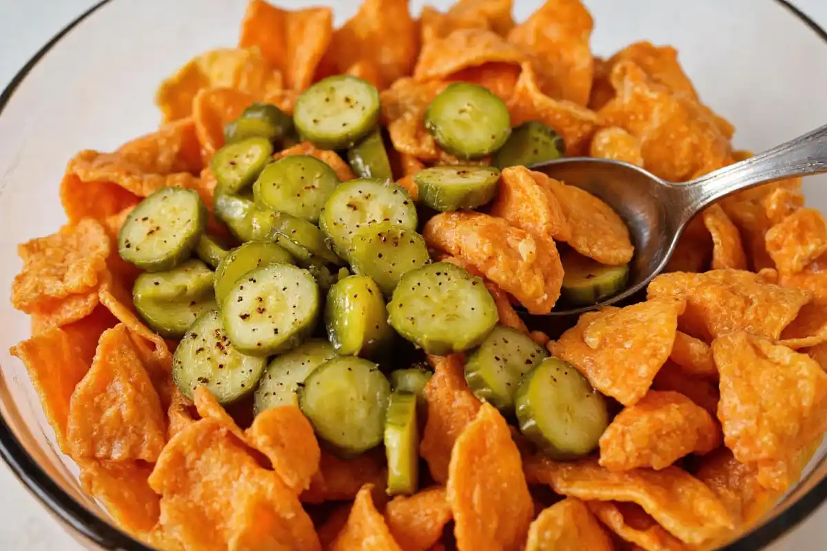 A bowl with Hot Cheetos and freshly chopped dill pickles being tossed together.