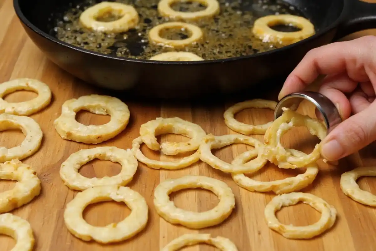 Potato rings being shaped and fried in a pan of hot oil.