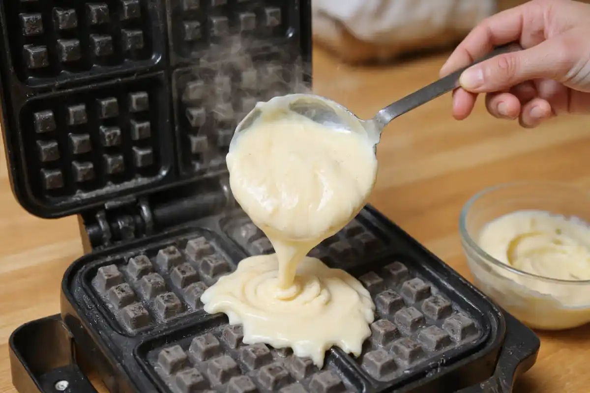 Smooth waffle batter being poured into a preheated waffle iron, creating a perfect even spread.