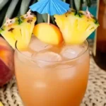 A tropical rum cocktail beach peach lemonade served with ice, peach and pineapple slices, and a blue paper umbrella
