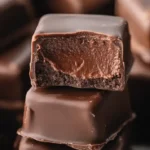 A Easy Cool Whip Candy stack of chocolate fudge squares with a smooth chocolate coating, one piece cut open to show the creamy filling inside