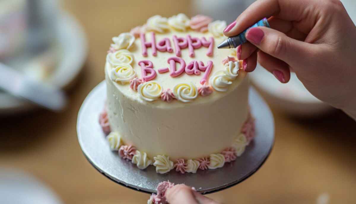 Hands decorating bento cake with pastel frosting and message