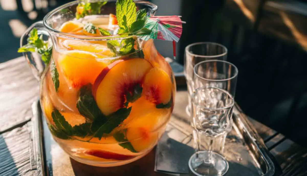 Pitcher of peach beach drink with fruit and mint garnish, party-ready
