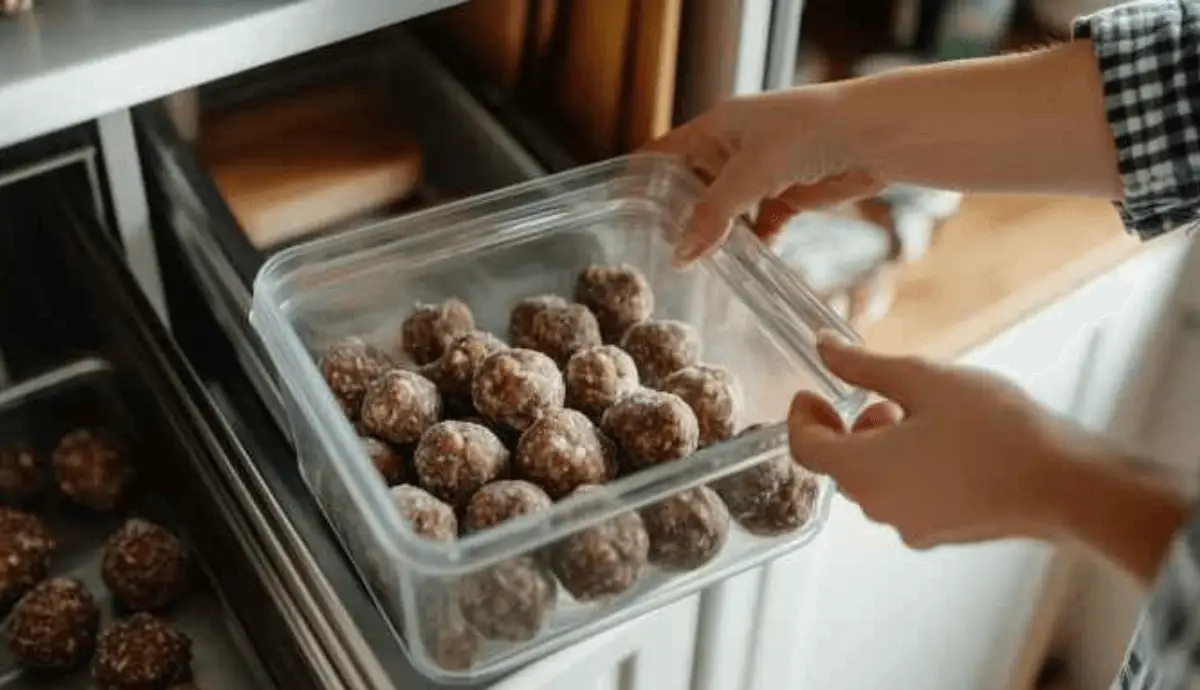 Airtight container of recipe for no bake butterfinger balls being placed into a refrigerator.