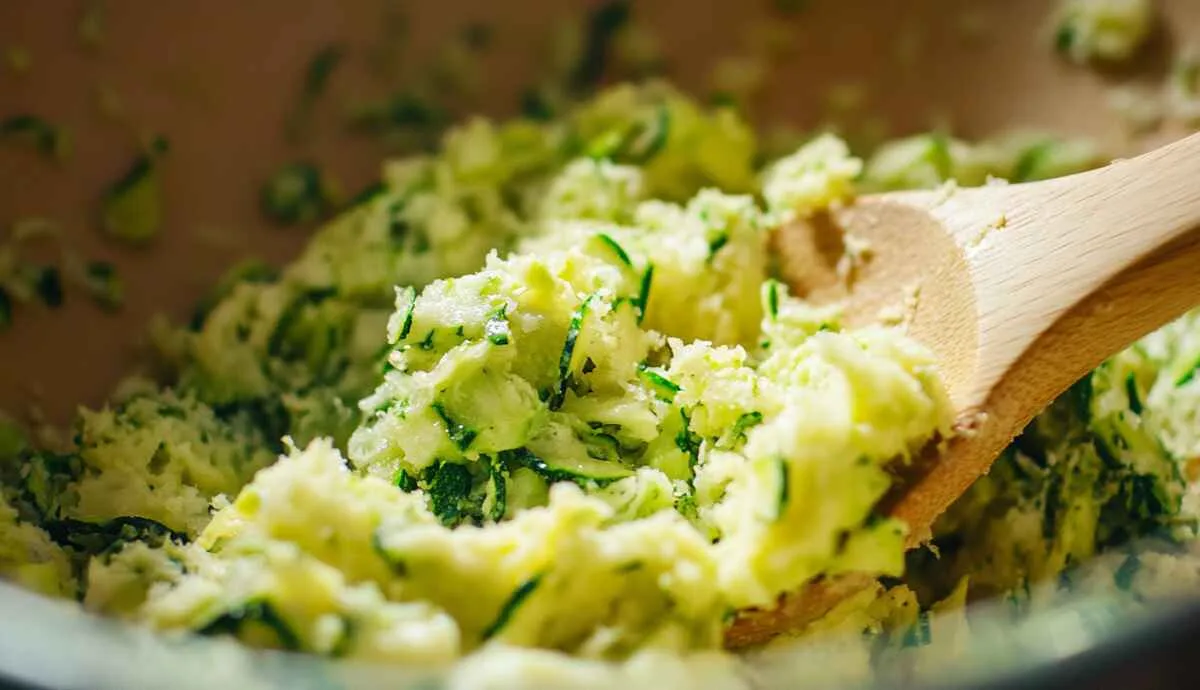 Grated zucchini being mixed into cake mix batter for a moist zucchini bread.