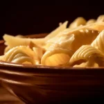A close-up shot of a rustic ceramic bowl filled with homemade garganelli pasta. The pasta is coated in a glistening brown butter and sage sauce and is garnished with a generous amount of freshly grated Parmesan cheese and a few crispy sage leaves.
