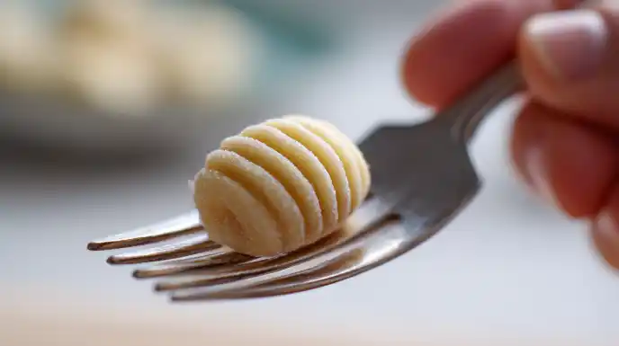 Close-up of gnocchi being shaped with a fork to create traditional ridges.